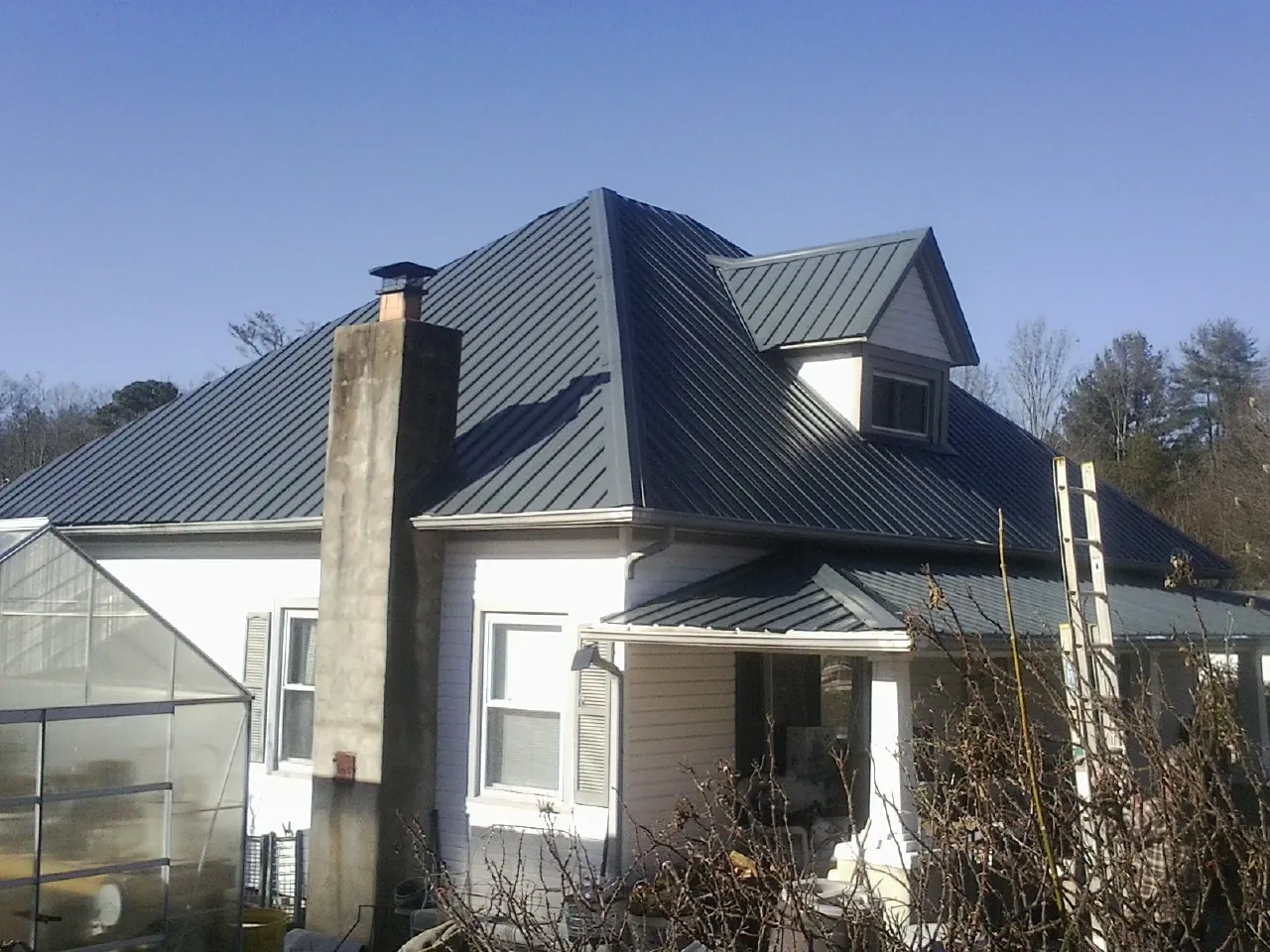 Dark blue standing seam metal roof on a white farmhouse with dormer — Slate & Tile Roof Repair by Roofing Brothers in Spartansburg