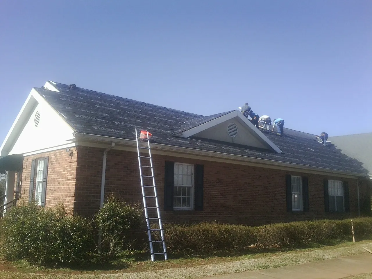 Crew tearing shingles off a brick ranch roof with a ladder set — Metal Roof Repair work by our crew in Spartansburg