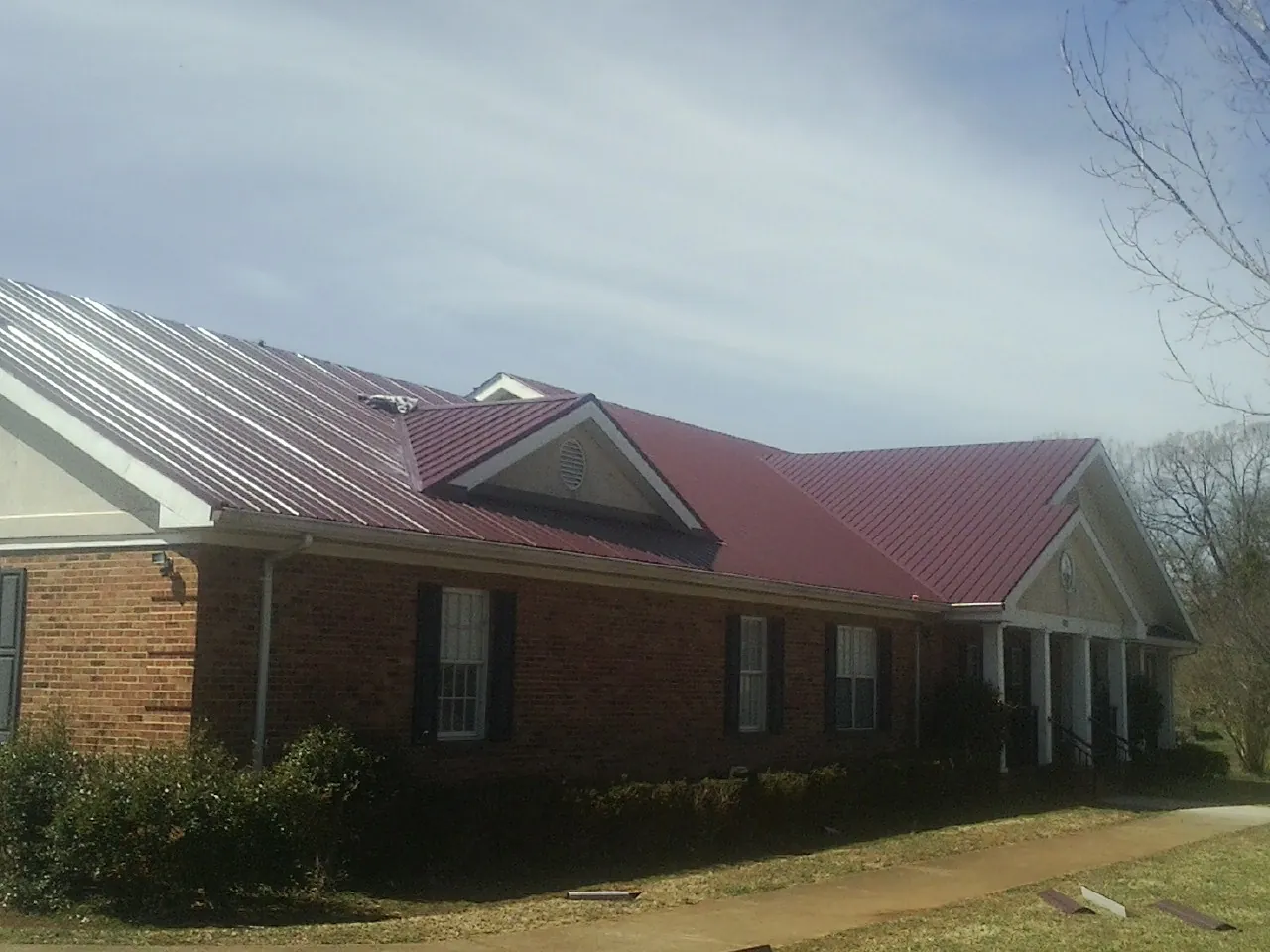 Red metal roof with gabled entries on a long brick building, from a Hail Damage Roof Repair job in Spartansburg