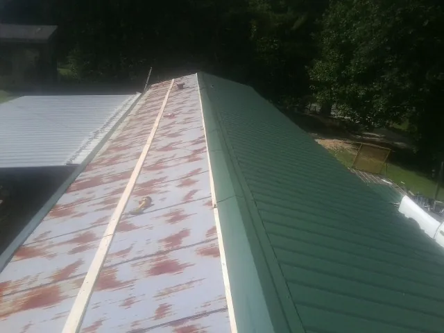 Old rusted panels beside newly installed green metal roofing — Wind Damage Roof Repair by Roofing Brothers in Spartansburg