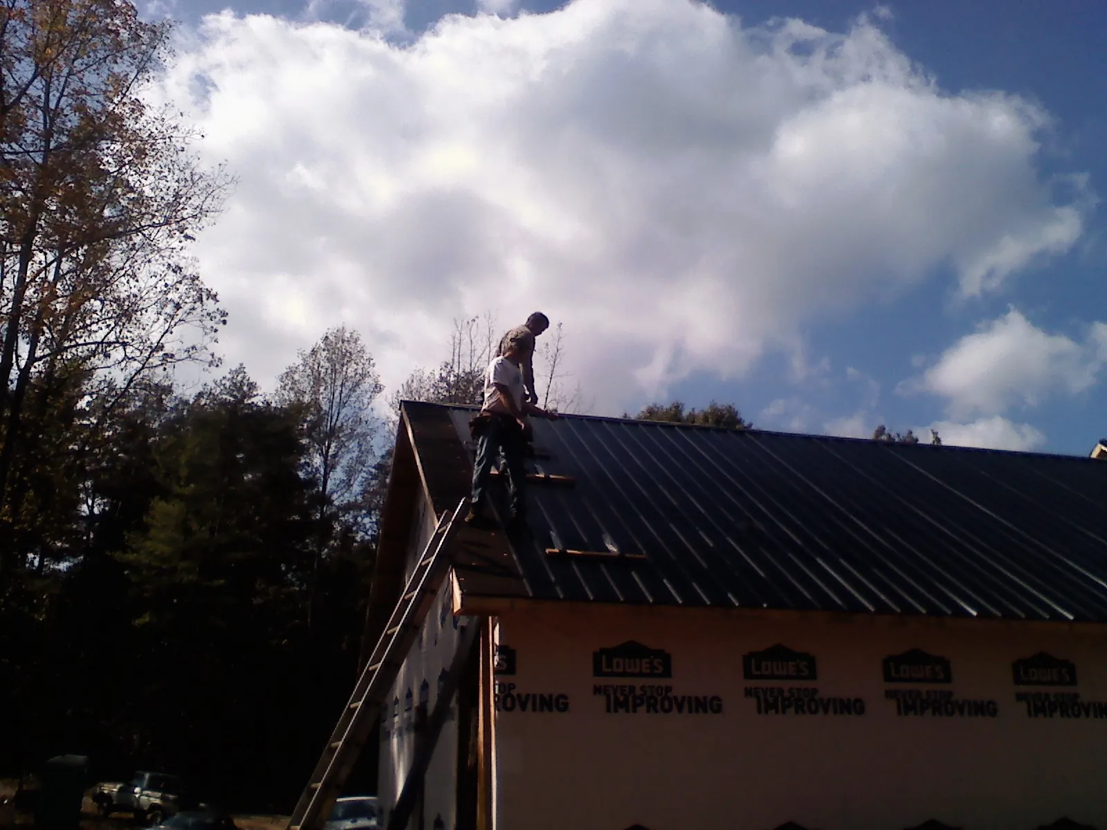 Roofer fastening dark metal panels high against a cloudy sky, from a Roof Inspection job in Spartansburg