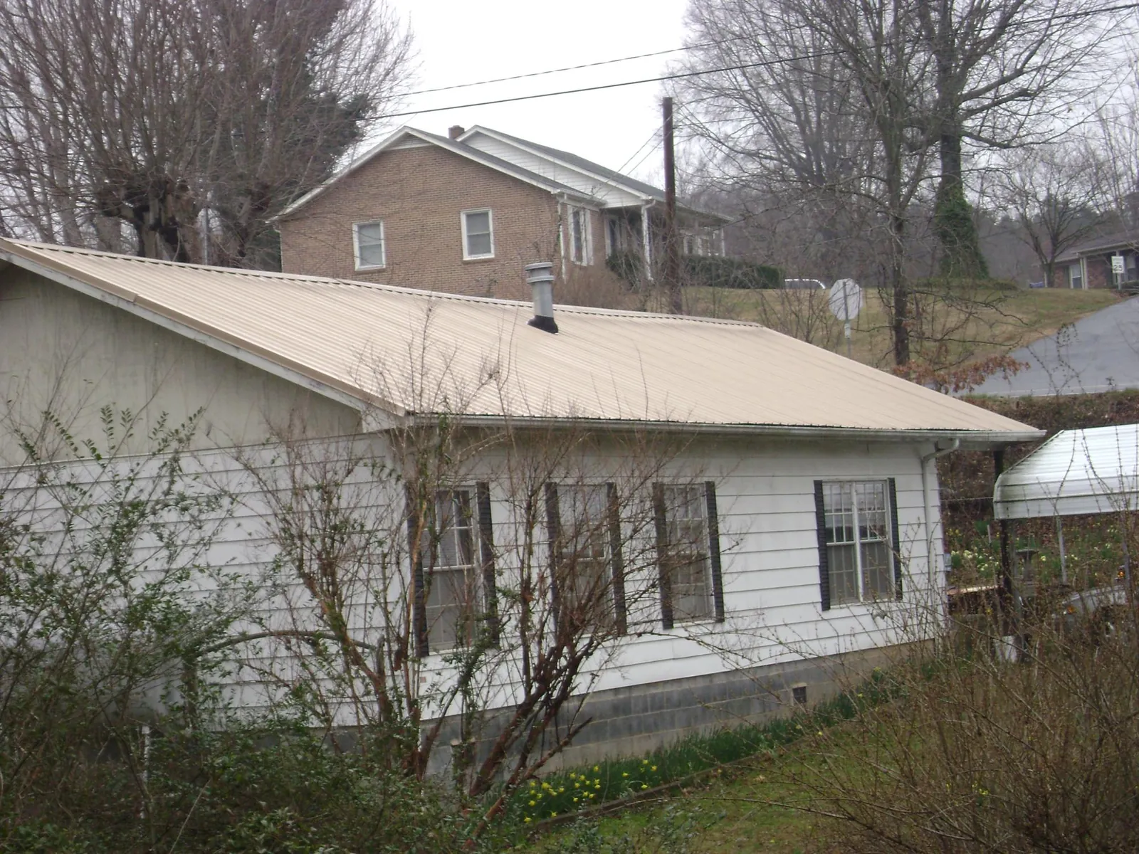 Tan metal roof on a white sided house set into a hillside — Commercial Roofing by Roofing Brothers in Spartansburg